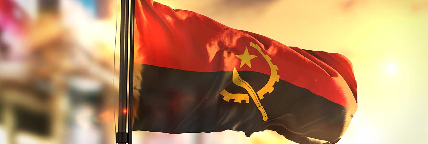 Angola flag against city blurred background at sunrise back light