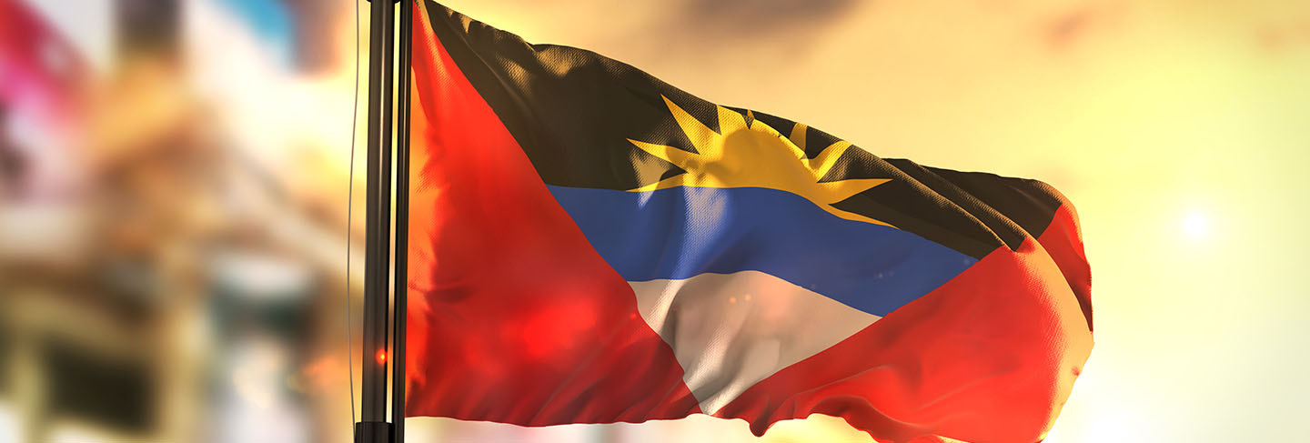 Antigua and barbuda flag against city blurred background at sunrise backlight