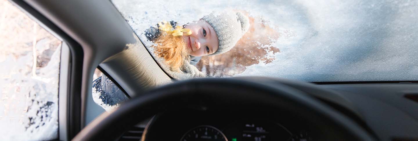 The kid helps and scraping snow and ice from car window