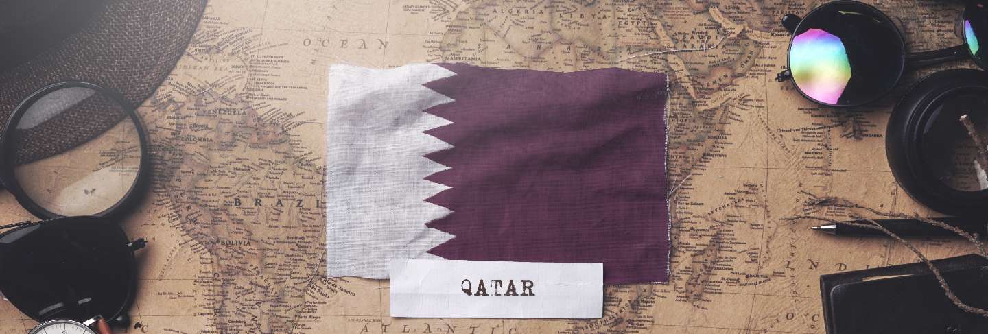 Qatar flag between traveler's accessories on old vintage map. overhead shot