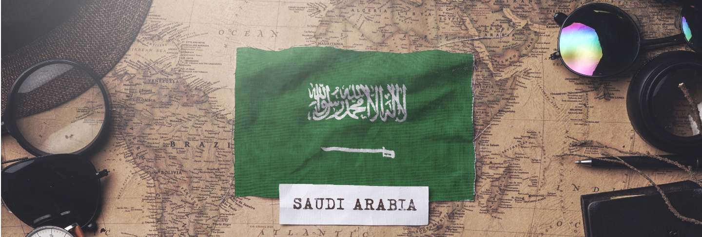 Saudi arabia flag between traveler's accessories on old vintage map. overhead shot 