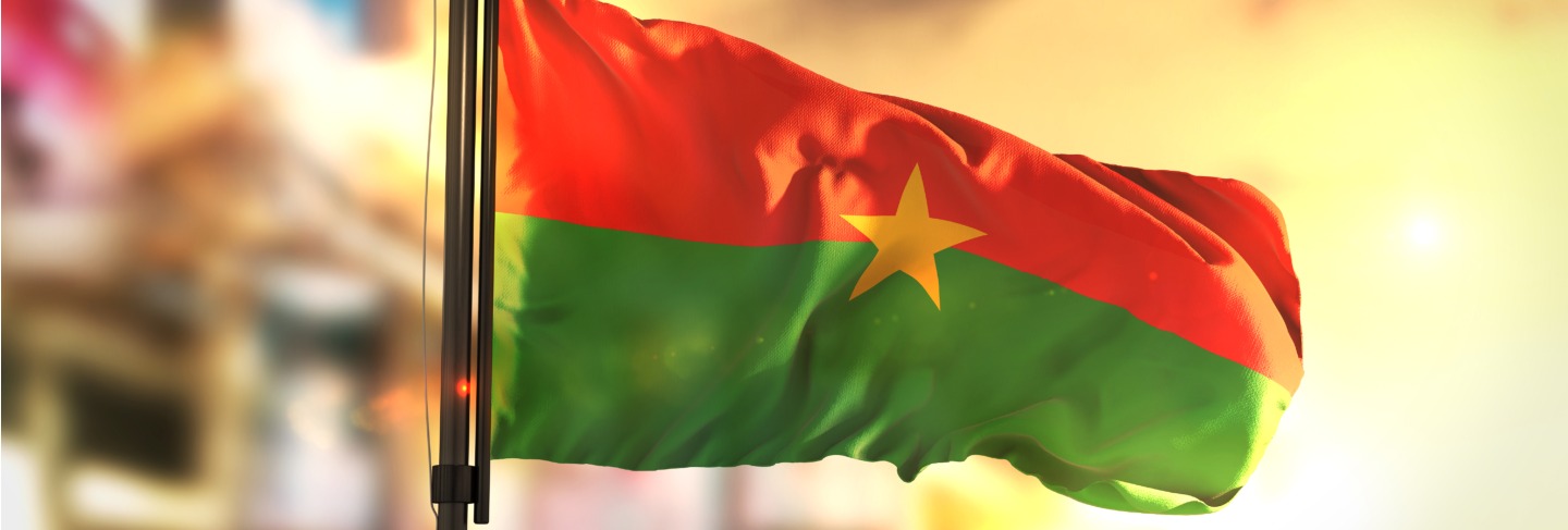 Burkina faso flag against city blurred background at sunrise backlight