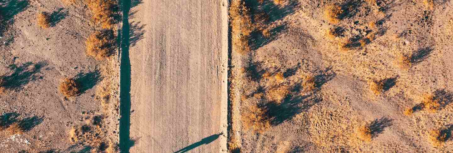 Overhead aerial drone shot of a narrow desert road with a car on the side of the road
