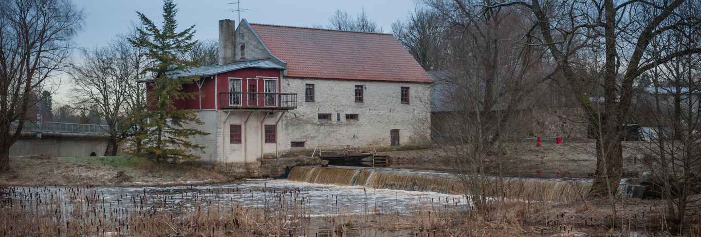 Old mill on the river bank with small waterfall at winter time
