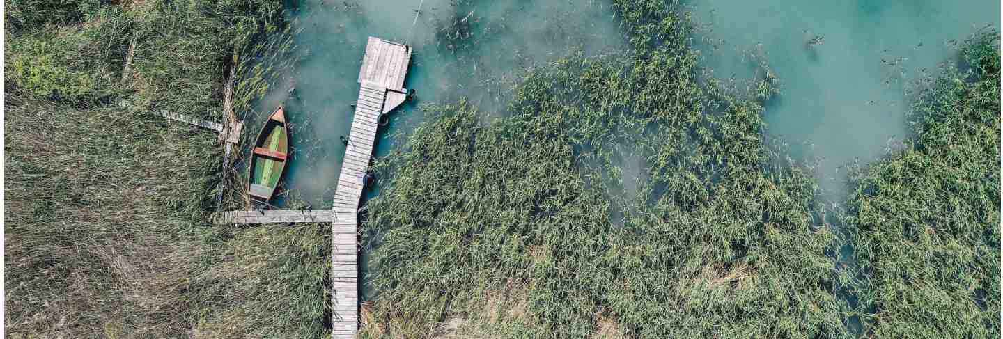 Overhead shot of a wooden dock at the coast with a fishing boat next to it 
