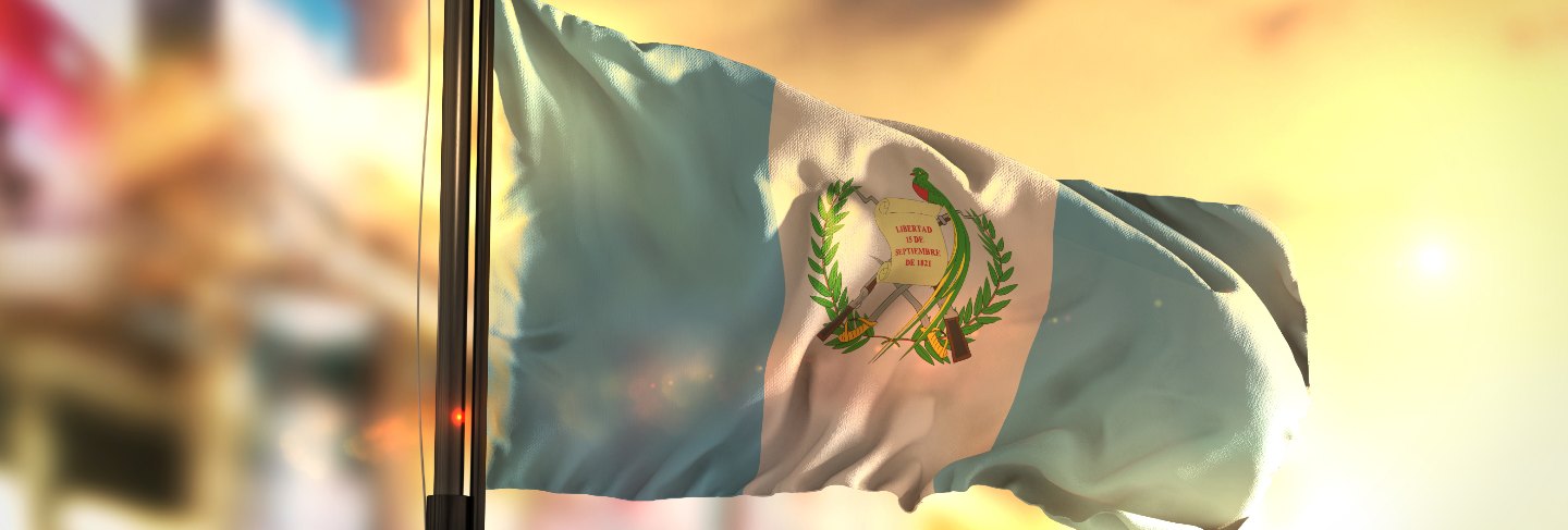 Guatemala flag against city blurred background at sunrise backlight
