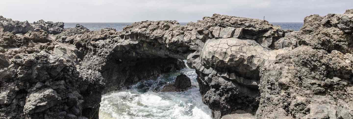 Wide shot of rock formations on the body of water under sky