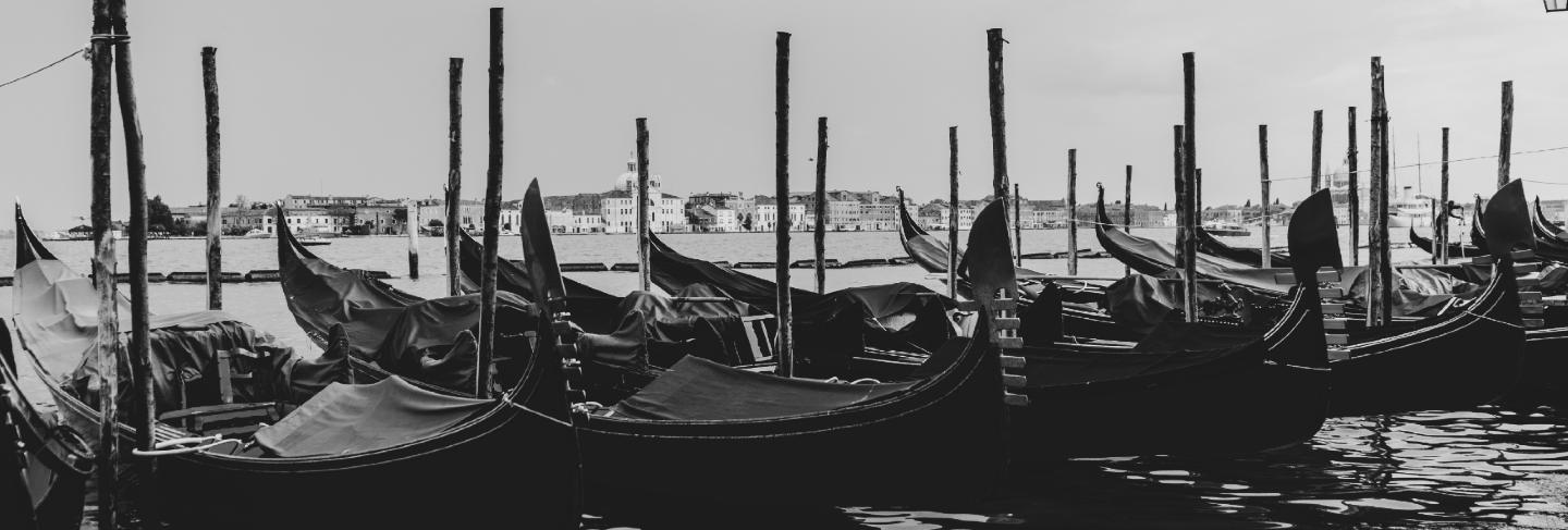 Black and white shot of gondolas docked in the water
