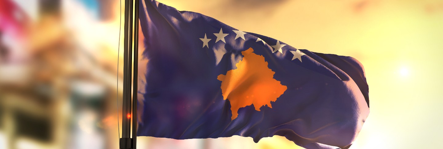 Kosovo flag against city blurred background at sunrise backlight
