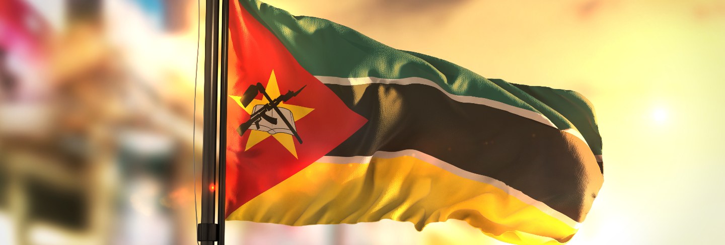 Mozambique flag against city blurred background at sunrise backlight

