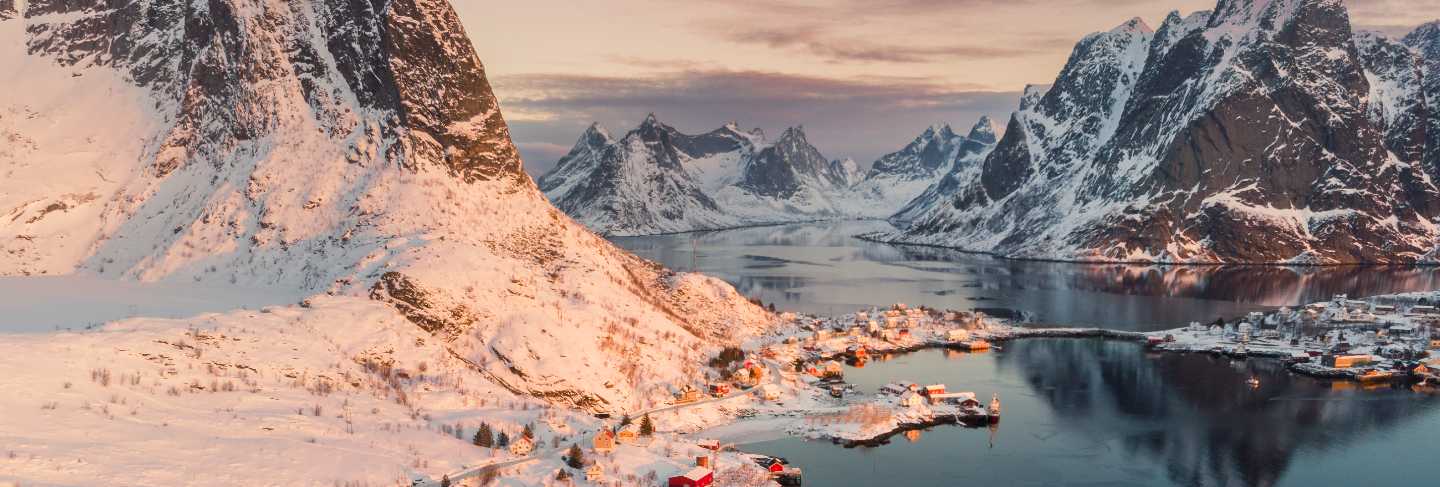 Aerial view of scandinavian village on coastline in snowy valley at sunset
