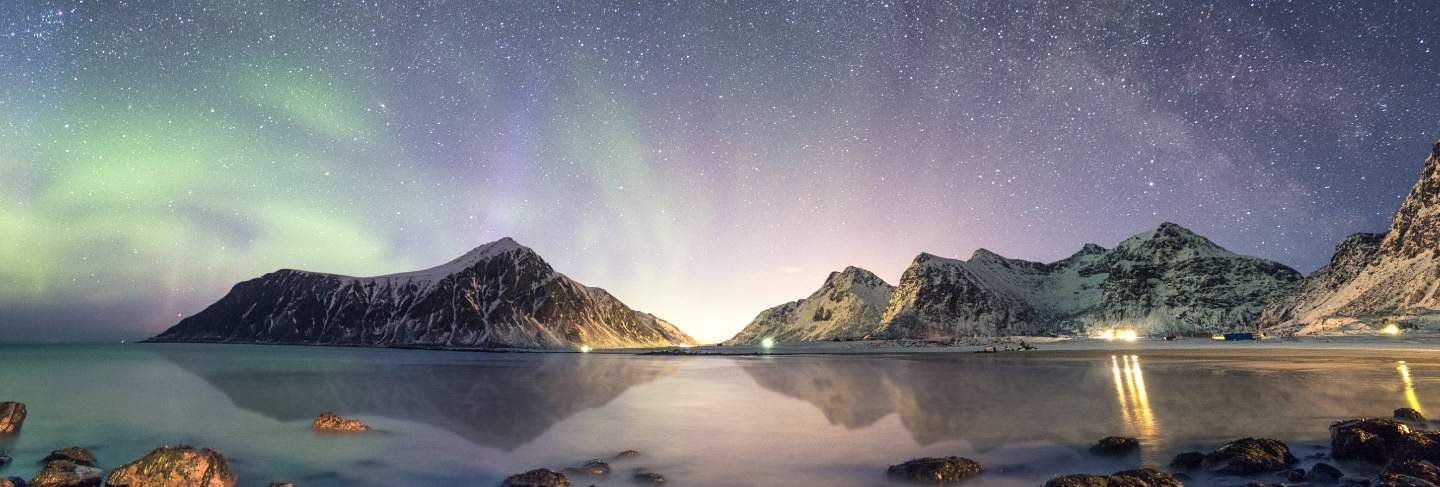 Panorama of aurora borealis with milky way galaxy over snow mountain in coastline
