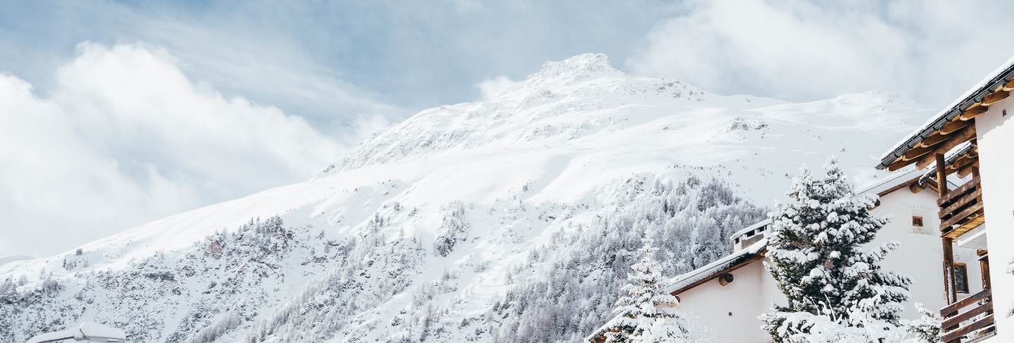 Wide shot of a white and brown house near trees and a mountain covered in snow 
