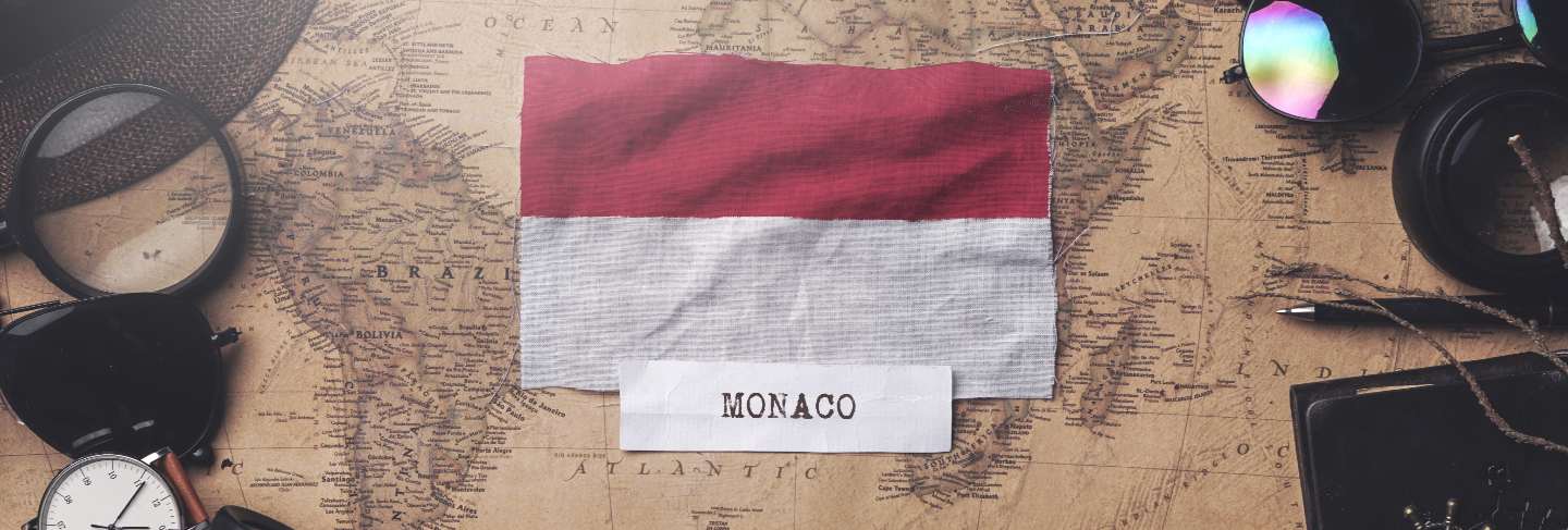  Monaco flag between traveler's accessories on old vintage map.