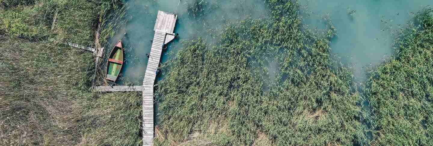 Overhead shot of a wooden dock at the coast with a fishing boat next to it
