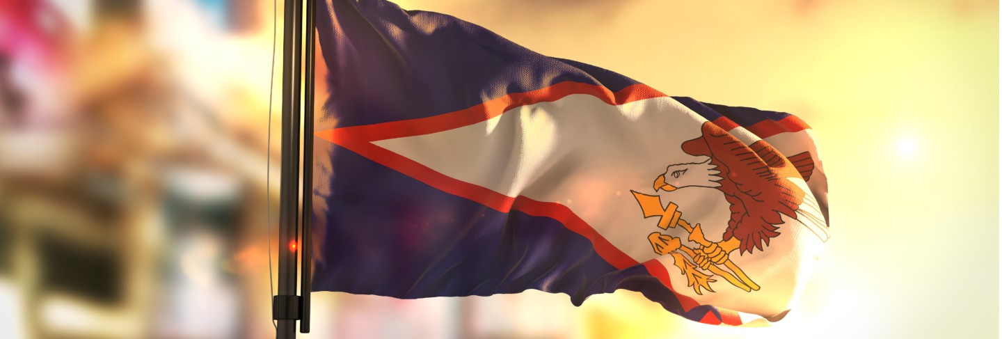 American samoa flag against city blurred background at sunrise backlight