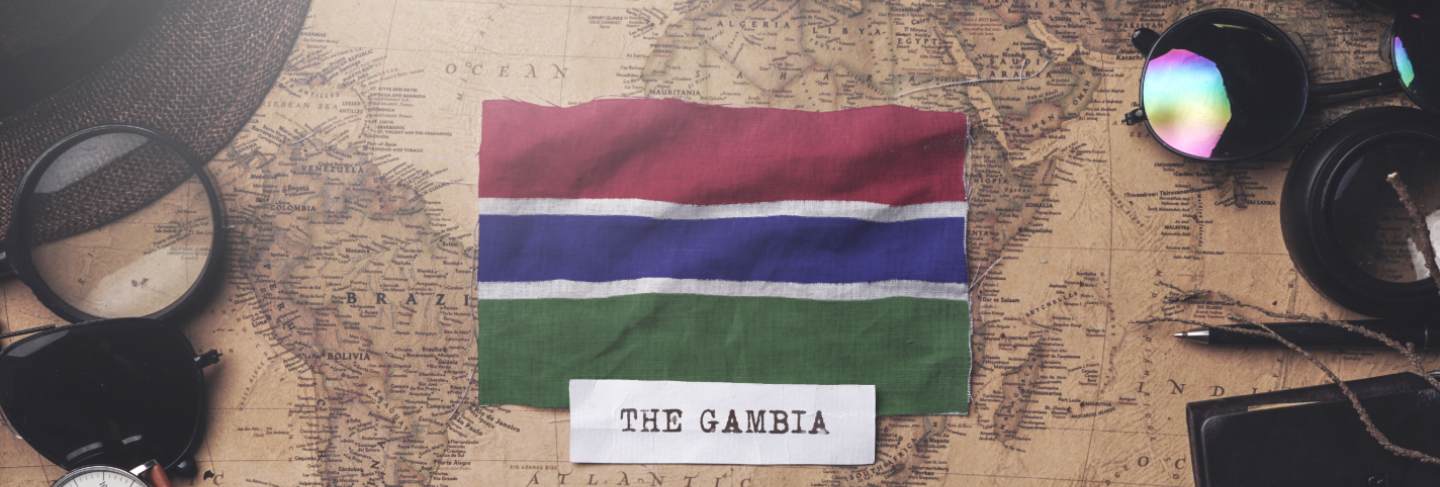 The gambia flag between traveler's accessories on old vintage map. overhead shot
