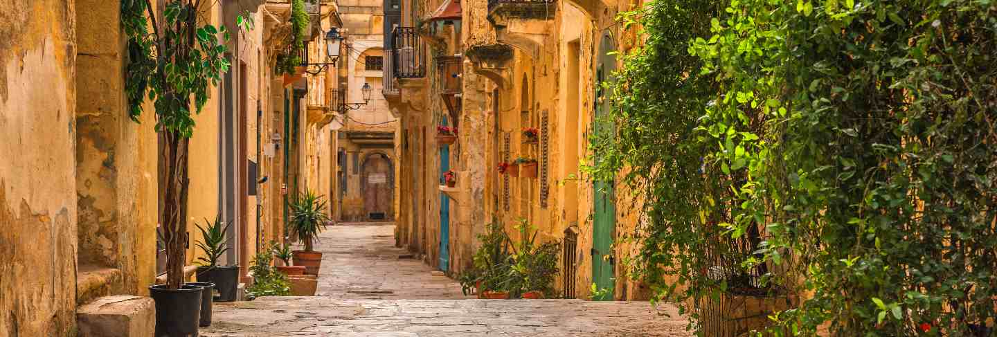 Valletta, malta. old medieval empty street with yellow buildings and flower pots Premium Photo
