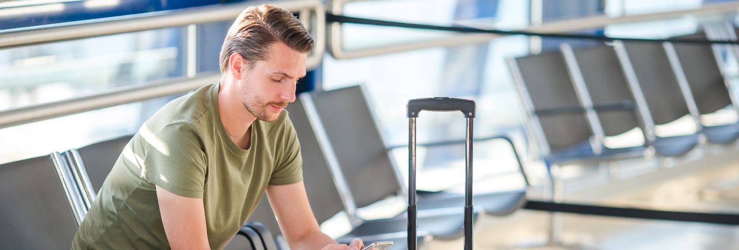 Passenger in a airport lounge waiting for flight aircraft, young man with cellphone in airport waiting for landing
