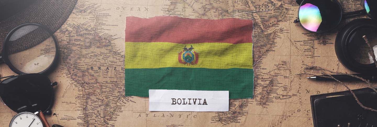 Bolivia flag between traveler's accessories on old vintage map.
