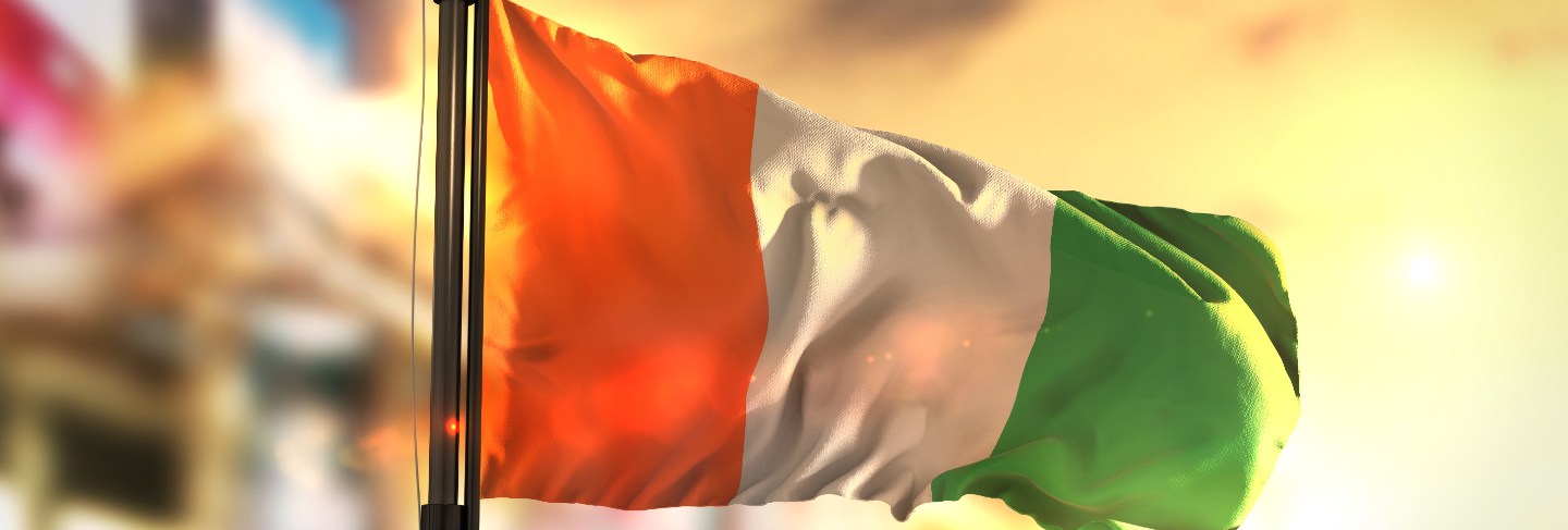 Ivory coast flag against city blurred background at sunrise backlight
