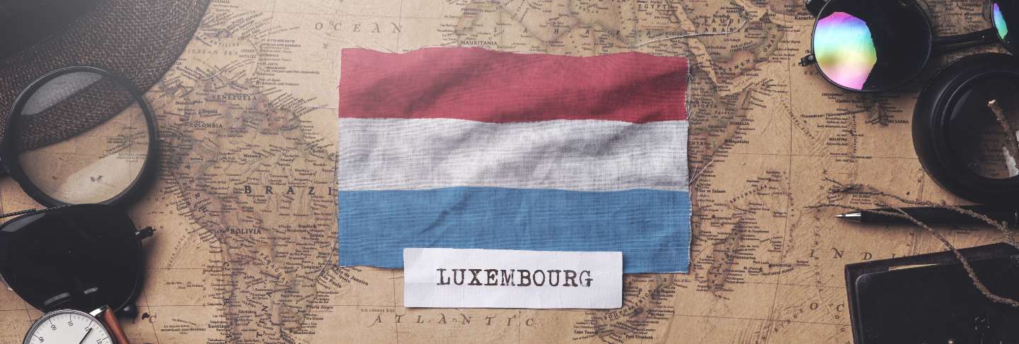 Luxembourg flag between traveler's accessories on old vintage map. overhead shot
