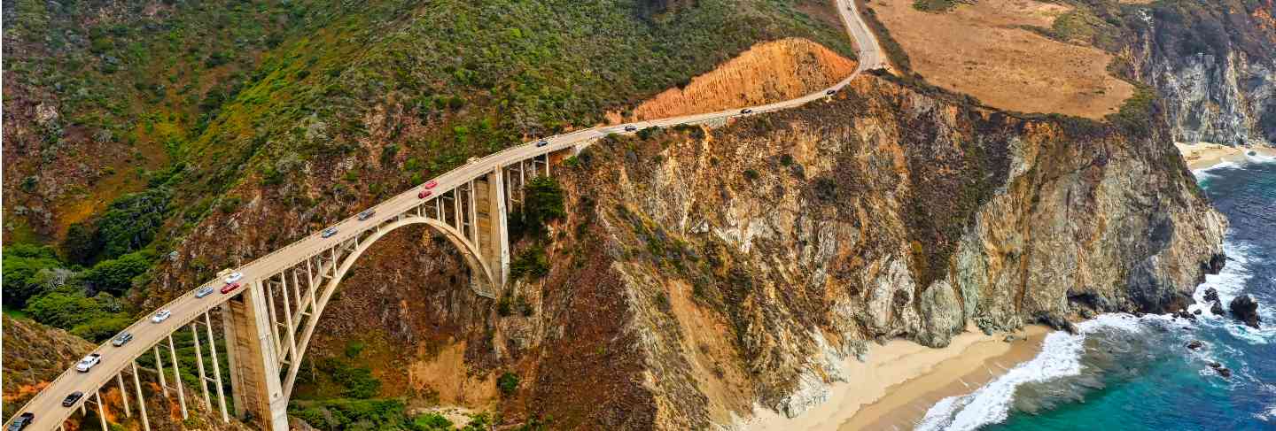 Beautiful aerial shot of green hills and a curvy narrow bridge going along the cliffs 
