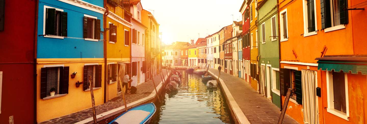 Beautiful sunset with boats, buildings and water. sun light. toning. burano, italy.
