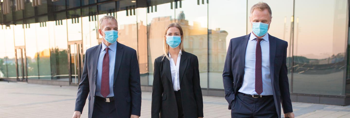 Business tourists in face masks visiting foreign partner office, wheeling suitcase, walking outdoors. front view. business trip and epidemic concept
