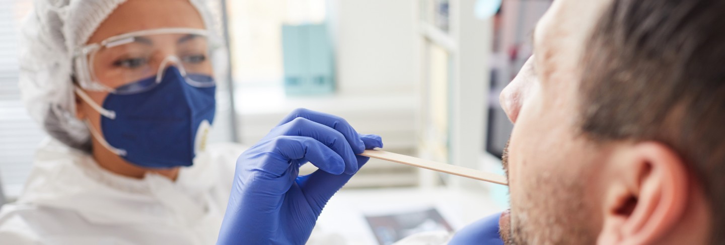 Mature man opening the mouth while doctor in protective clothing examining his throat during medical exam at hospital
