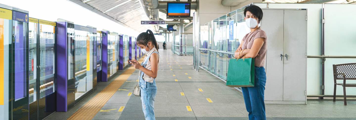 Asian woman keep distance to other people in empty subway platform
