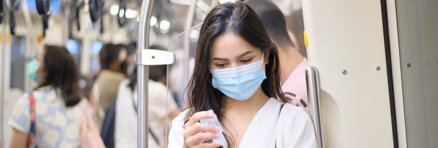 A young woman wearing protective mask in subway is using alcohol to wash hands, travel under covid-19 pandemic, safety travels, social distancing protocol
