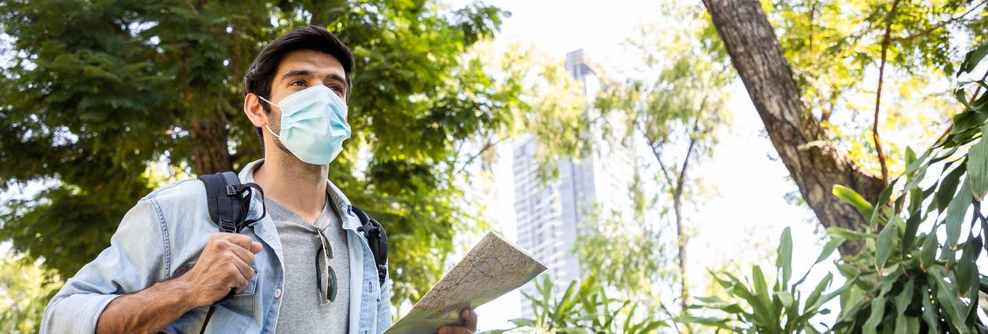 Young handsome man looking paper map and using sun glasses in public park with a happy face standing and smiling
