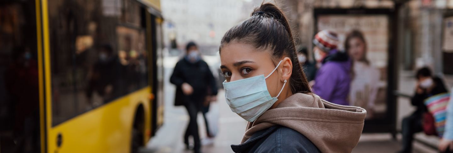 Young woman wearing surgical mask outdoor at bus stop in the street
